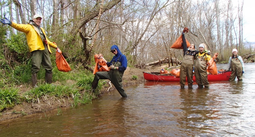 A group of people stand in or near ankle-deep water holding bags of trash. 